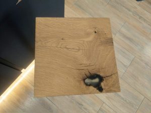 Square wooden plank with visible grain and a dark hole, a sample for custom tables and doors.