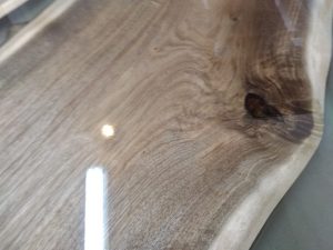 Polished live-edge wooden table top slab with visible grain and a knot.