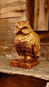 Hand-carved wooden owl statue on a rustic wooden surface, showcasing craftsmanship for custom tables and doors.