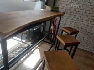 Handcrafted live-edge wooden counter with a metal frame and accompanying wooden stools in a showroom.