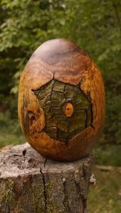 Hand-carved wooden egg with a dark geometric pattern and orange center sits on a tree stump, showcasing skilled woodcraft for handcrafted tables and doors.