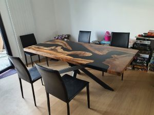 Handcrafted live-edge wooden dining table with epoxy resin inlay and black metal legs, showcased in a showroom for custom wooden tables and doors.