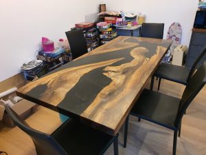 A long, handcrafted wooden table with dramatic grain and epoxy accents, shown in a workshop, showcasing our custom-made wooden tables and doors.