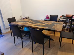 Showroom for a woodworking company specializing in custom wooden tables and doors, featuring a long handcrafted dining table with a contrasting inlay surrounded by black chairs.