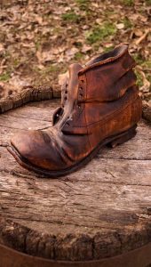 A weathered brown leather boot rests on a rustic wooden stump outdoors, highlighting the natural wood texture featured in our handcrafted tables and doors.