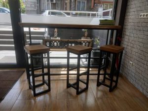 Showroom display of handcrafted wooden bar-height table with three matching stools on black metal frames, highlighting premium timber furniture.