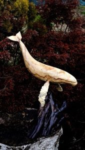 Hand-carved wooden whale sculpture perched on a rock, illustrating artisanal woodwork for tables, doors, and décor.