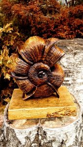 Handcrafted wooden flower sculpture on a rustic pedestal atop a tree stump, showcasing our handmade wooden tables and doors.