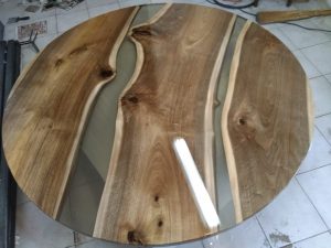 Round live-edge wooden table top with epoxy resin inlays, highlighting natural grain for a handcrafted furniture business making tables and doors.