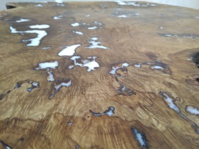 Close-up of a rustic wooden tabletop with prominent grain and pale patches, highlighting handcrafted tables and doors.