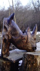 Hand-carved wooden rhino head sculpture outdoors, showcasing the timber craftsmanship behind our wooden tables and doors.