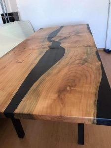 Handcrafted wooden dining table with a black resin river inlay and natural wood grain, supported by dark legs.
