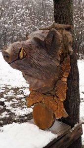 Hand-carved wooden pig head with leaf accents, showcasing artisanal timberwork for rustic tables and doors.