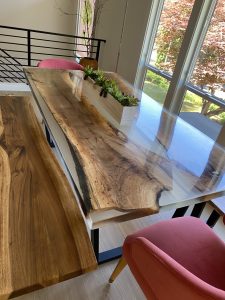 Handcrafted live-edge wooden dining table with natural grain and a greenery centerpiece in a sunlit room, showcasing our custom wooden tables.