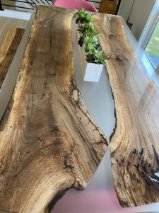 Two large live-edge wooden table slabs with natural grain and a small potted plant centerpiece.