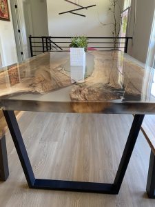 Handcrafted wooden dining table with a glossy natural wood grain top and black metal legs, part of our custom wooden tables and doors collection.