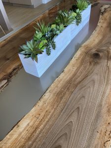 Close-up of a handcrafted live-edge wooden table with bold grain, next to a white rectangular planter filled with green succulents.