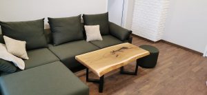 Cozy living room featuring a natural wood coffee table and a green sectional sofa on a wooden floor, showcasing handcrafted wooden furniture for homes.