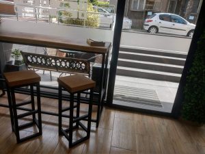 Indoor showroom featuring a handcrafted wooden bar-height table with two stools beside a glass storefront door.