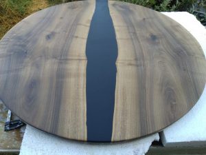 Round wooden table top with a dark epoxy resin river running through the center, highlighting natural wood grain.