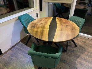 Handcrafted round live-edge wooden dining table with a black epoxy river seam, paired with green upholstered chairs.