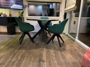 Showroom scene featuring a round wooden dining table with four green chairs, showcasing handcrafted wooden tables for homes and offices.