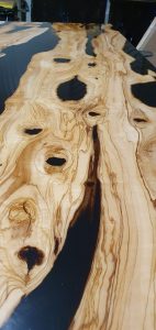 Live-edge wooden slab with dramatic grain, natural holes, and resin accents on a glossy surface, ideal for handcrafted tables and doors.
