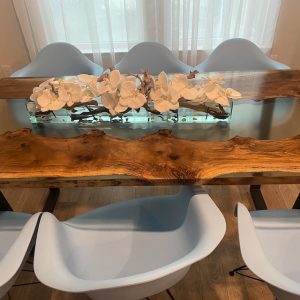Handcrafted live-edge wooden dining table with a glass top and a white floral centerpiece.
