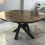 Round wooden dining table with a dark finish and crisscross pedestal base on display in a showroom for a wood furniture company.