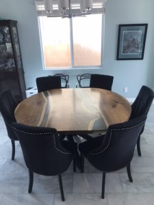 Round handcrafted wooden dining table with six black upholstered chairs, showcasing solid-wood tables and doors.