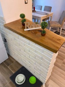 Handcrafted wooden furniture display in a showroom, featuring a wooden counter with a light brick base and a dining table set, showcasing the business's wooden tables and doors.