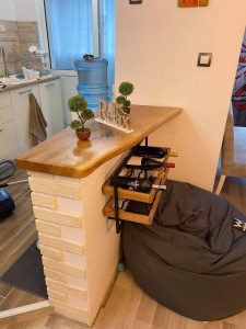 Showroom corner with a polished wooden bar-height counter on a white brick base, small potted plants, and a bean bag, highlighting handcrafted wooden tables and doors.