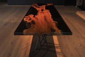 Handcrafted live-edge wooden dining table with a warm grain on a metal base, showcasing a woodworking company that makes tables and doors.