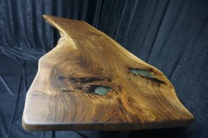 Live-edge wooden table top with turquoise resin inlays, highlighting natural grain for custom tables and doors.