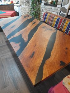 Handcrafted live-edge wooden dining table with a black epoxy river running through warm-toned planks, showcasing custom furniture from a woodworks business.