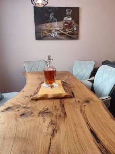 Handcrafted live-edge wooden dining table with a bottle and glass centerpiece on a napkin, showcasing our custom wooden tables in a modern dining room.