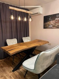 Showroom-style scene with a handcrafted live-edge wooden dining table and gray upholstered chairs under pendant lights.