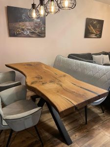 Live-edge wooden dining table with black metal legs in a modern showroom, representing a business that makes custom wooden tables and doors.