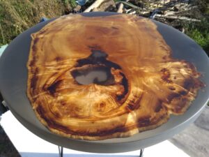 Round live-edge wooden table top with dramatic burl grain and a dark central knot, showcasing handcrafted timber furniture.