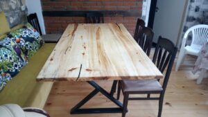 Handcrafted light pine dining table with a black metal base in a showroom, surrounded by wooden chairs.