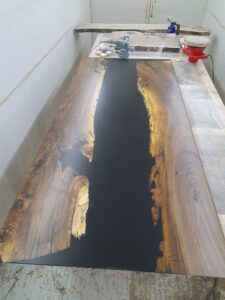 Custom wooden table top with a black epoxy river inlay being crafted in a woodworking shop.