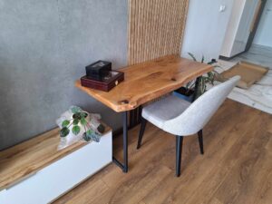 Handcrafted live-edge wooden table with black metal legs in a modern showroom, paired with a gray upholstered chair and a potted plant.