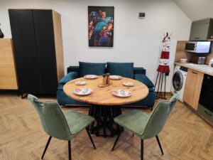 Showroom display of handcrafted wooden tables and doors from a furniture maker, featuring a round dining table with six green-upholstered chairs.