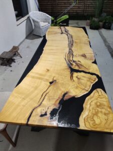 Handcrafted live-edge wooden dining table with a dark epoxy resin river running through the center, highlighting natural grain for custom tables and doors.