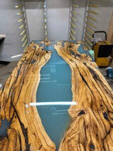 Custom live-edge wooden table with a blue epoxy river, built by our shop specializing in handmade tables and doors.