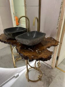 Handcrafted live-edge wooden bathroom vanity with two stone vessel sinks and gold fixtures, showcasing our custom wooden tables and doors.