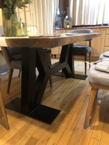 Handcrafted live-edge wooden dining table with a black metal base, built by our woodworking shop specializing in custom tables and doors.