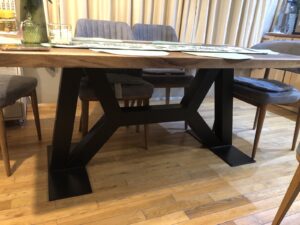 Handcrafted solid wood dining table with a chunky black base, showcased in a showroom for custom wooden tables and doors.