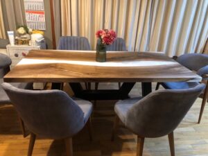 Handcrafted wooden dining table with six gray upholstered chairs in a warm room, showcasing a furniture maker’s wooden tables and doors.