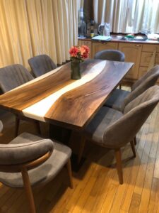 Handcrafted live-edge wooden dining table with upholstered chairs in a showroom, highlighting the company’s wooden tables and doors.